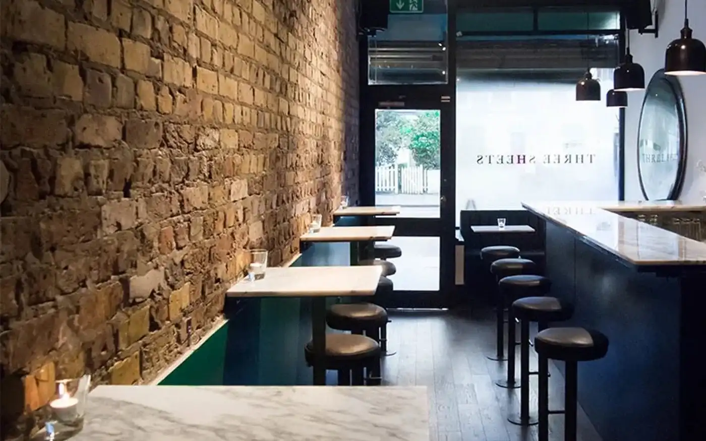 Brick wall, marble tables and stools inside Three Sheets cocktail bar in Dalston, London