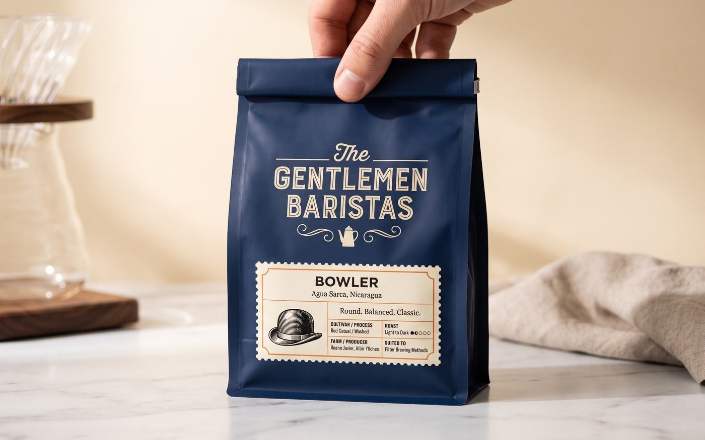 The Gentlemen Baristas Bowler single-origin Nicaraguan coffee beans in a navy bag, held above a marble counter