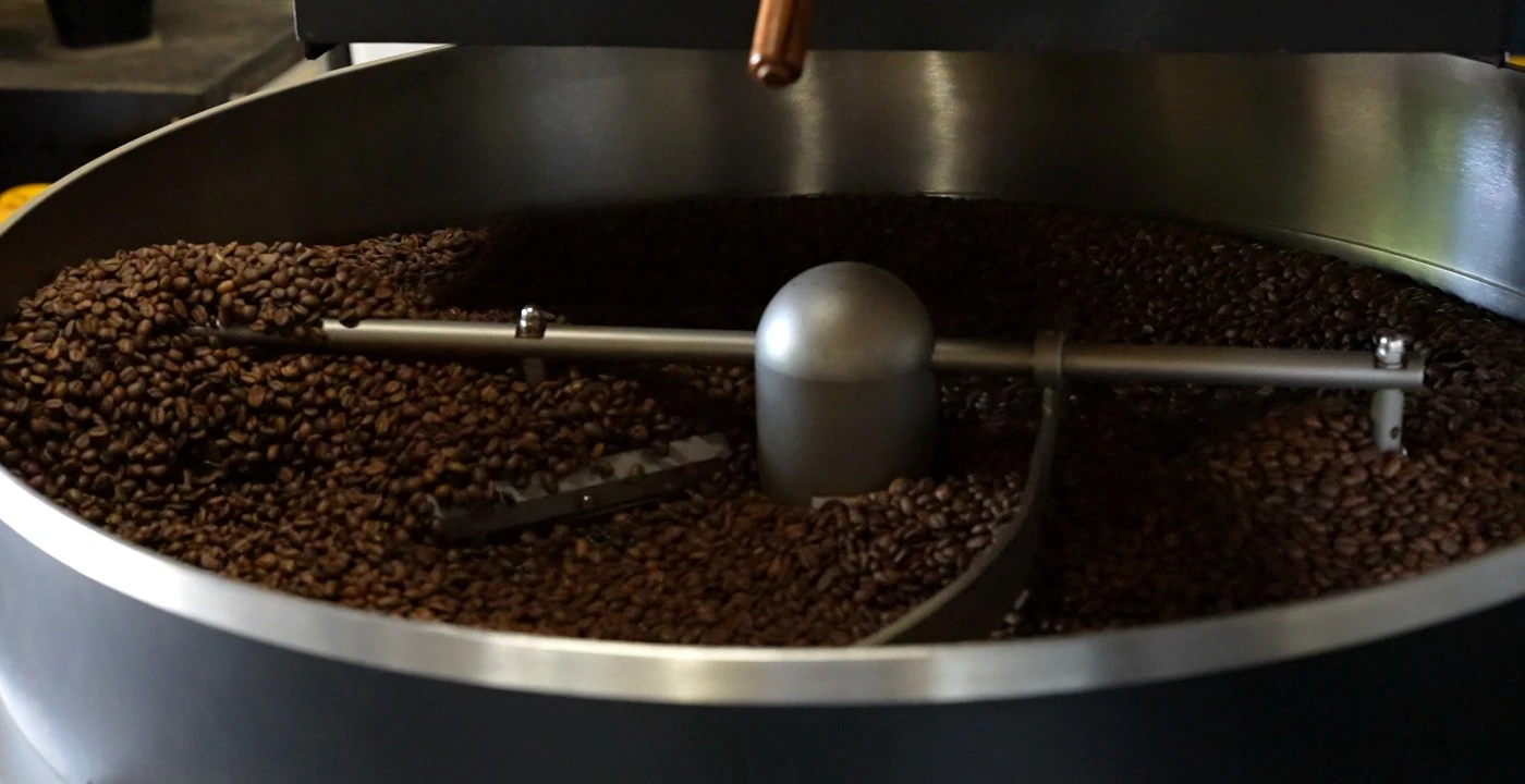 Freshly roasted coffee beans turning in the cooling tray of a drum roaster at a UK speciality roastery