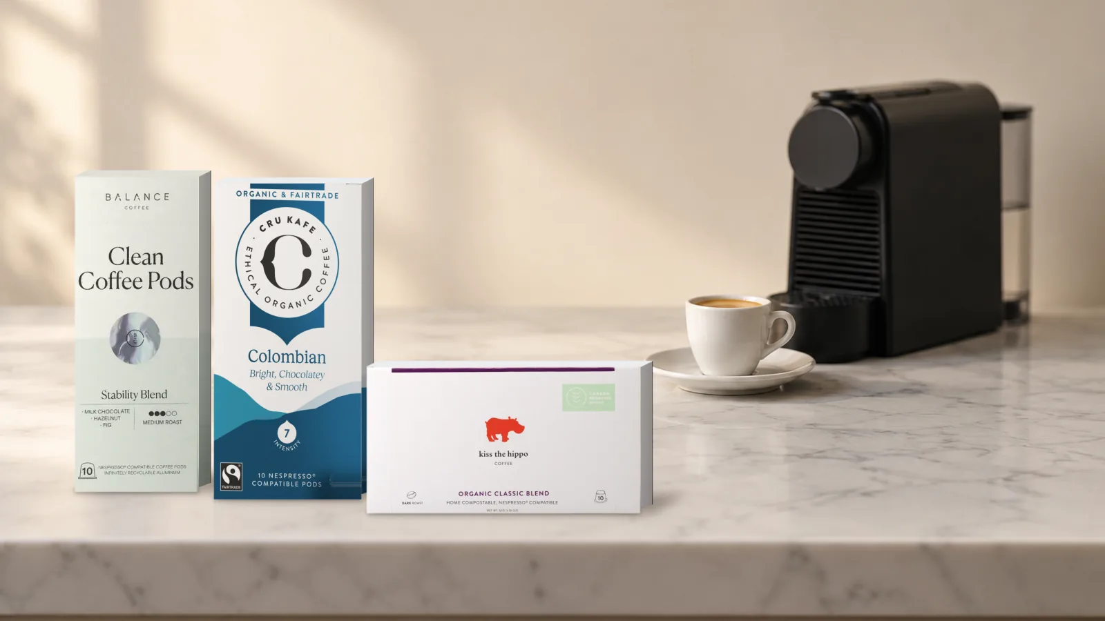Balance Coffee Clean Coffee Pods, CRU Kafe Organic Colombian and Kiss the Hippo Organic Classic Blend pod boxes beside a Nespresso machine