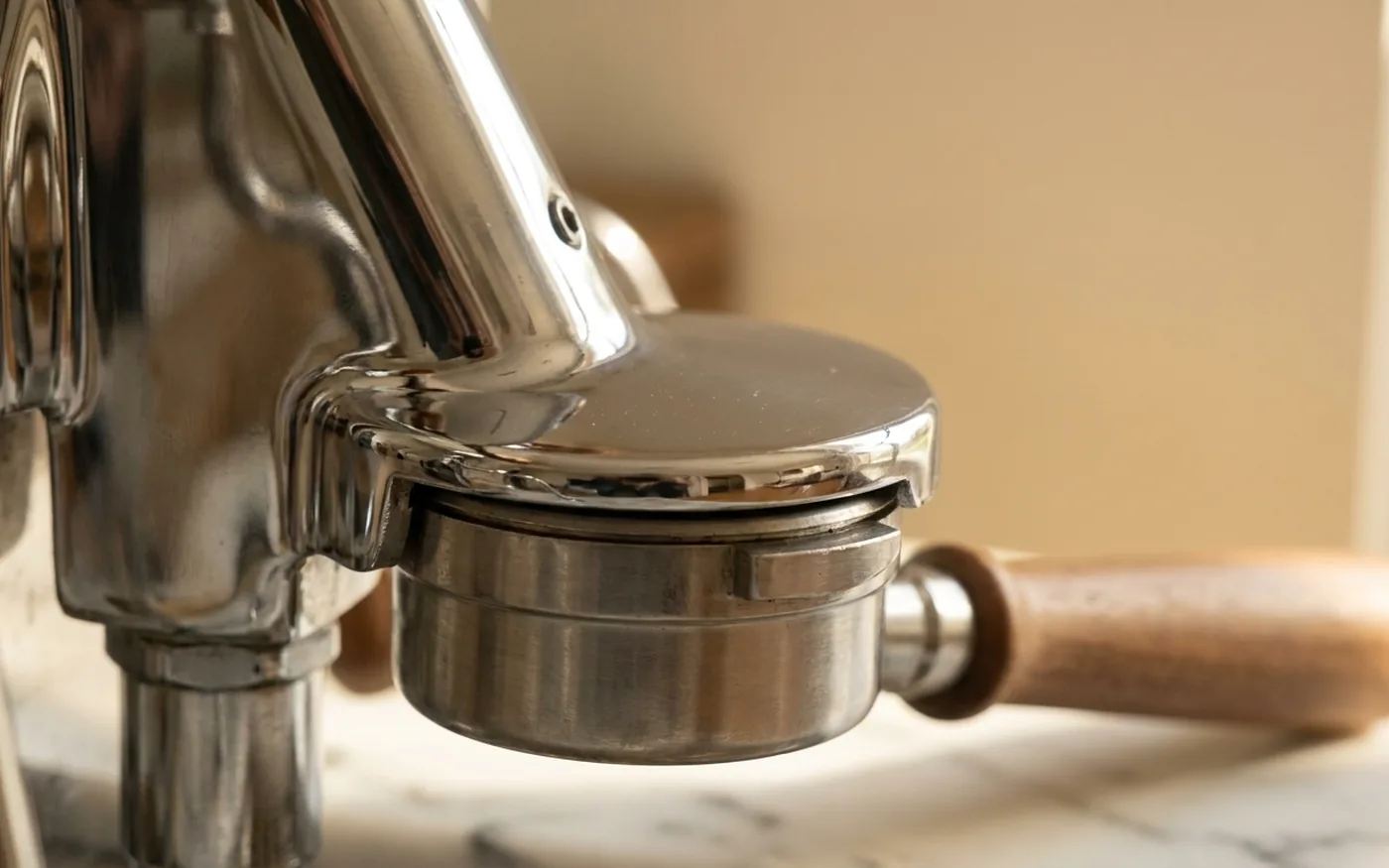 Close-up of a polished chrome E61 group head and stainless steel portafilter with a wooden handle