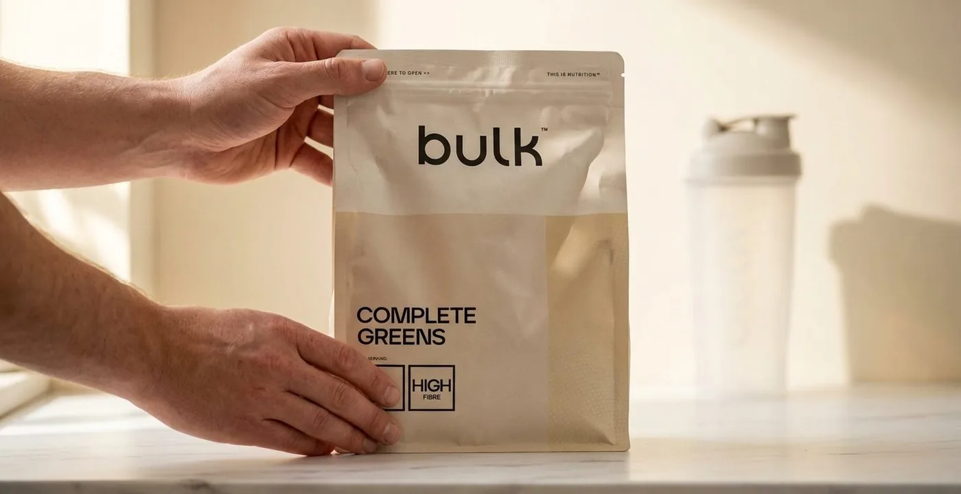 Bulk Complete Greens powder pouch on a white marble surface with shaker bottle
