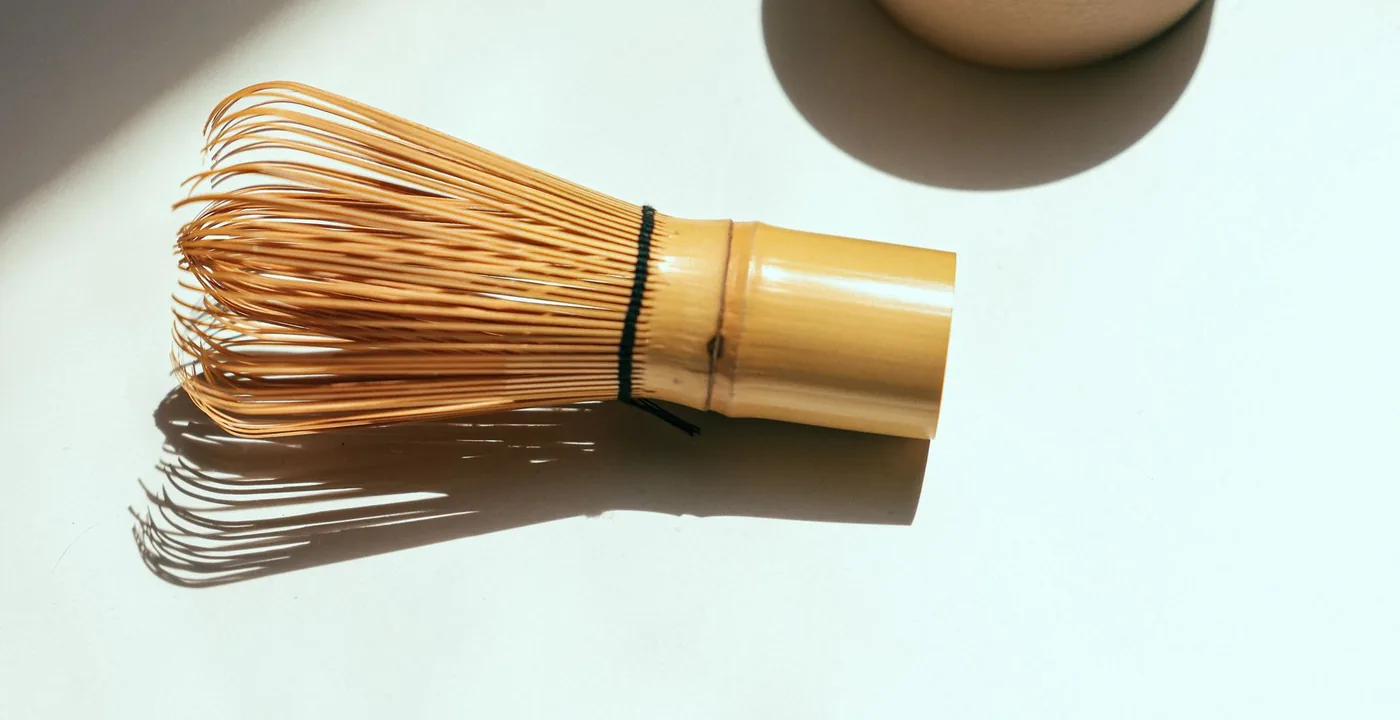 Matcha powder in a ceramic bowl with a bamboo whisk on a wooden surface