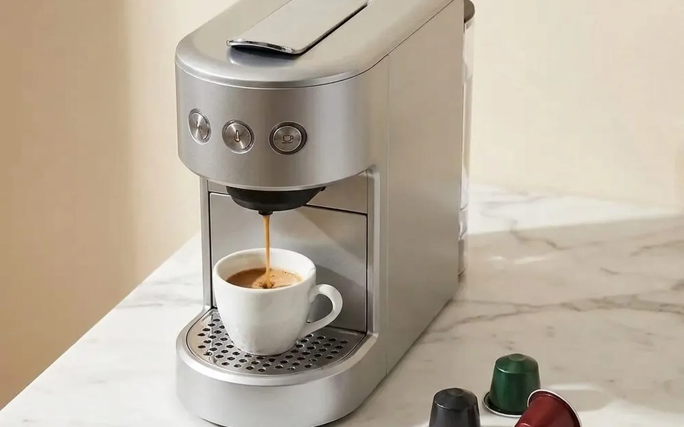 Compact Nespresso-style espresso machine on white marble kitchen counter with coffee capsules and espresso cup