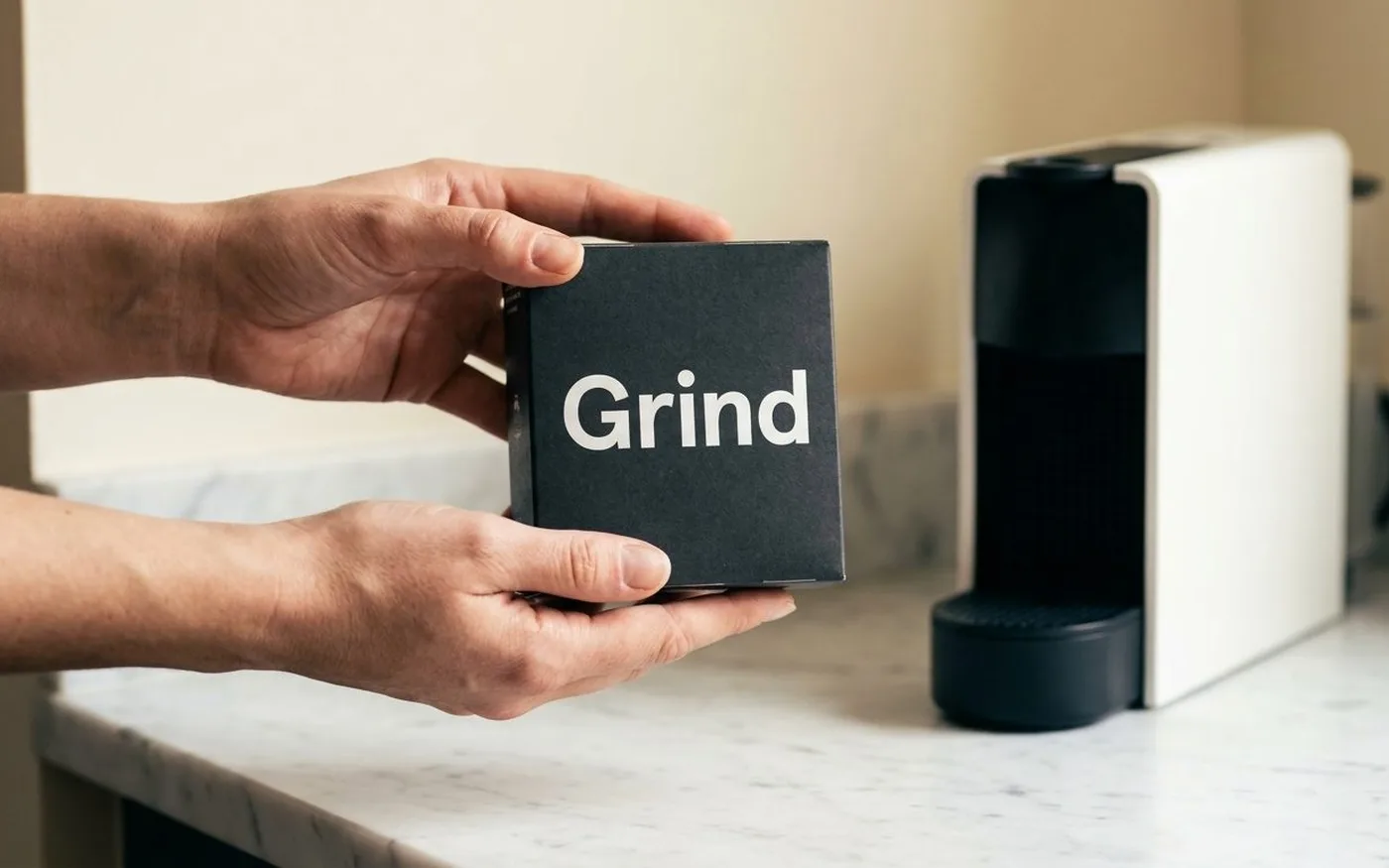 Grind compostable coffee pods on a white marble surface with a Nespresso machine in the background