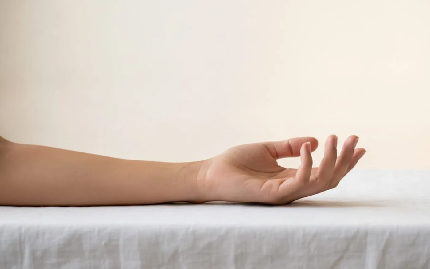 Relaxed forearm and hand resting on white linen illustrating muscle relaxation