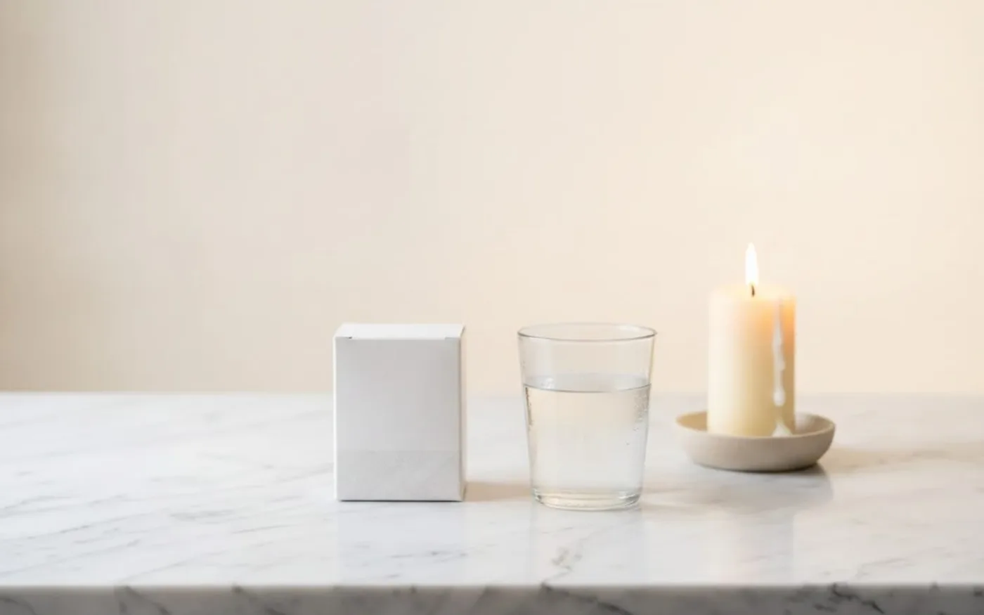 Supplement box, water glass and candle on marble surface representing an evening sleep routine