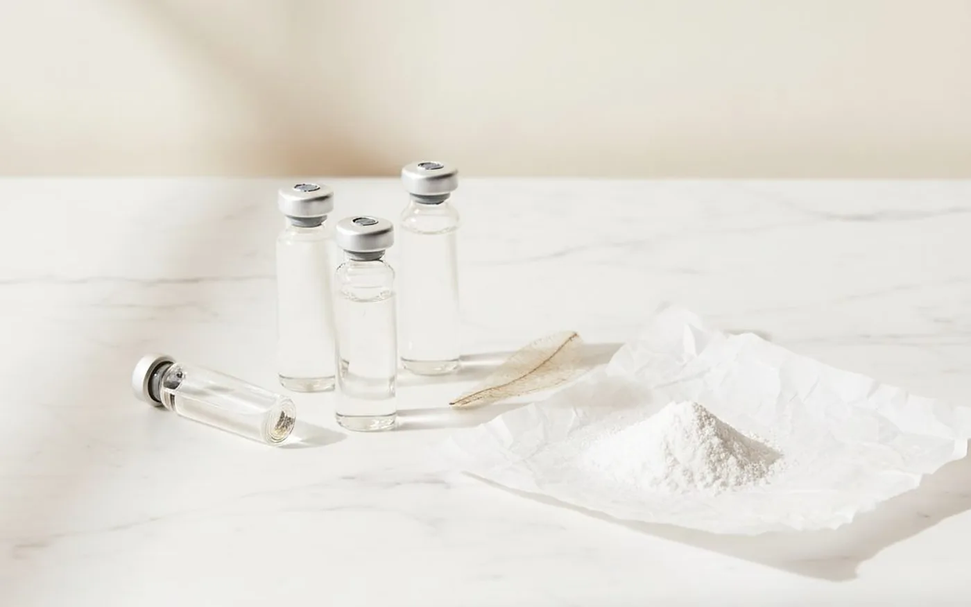 Glass vials and white collagen powder on white marble - representing hydrolysed marine collagen peptides