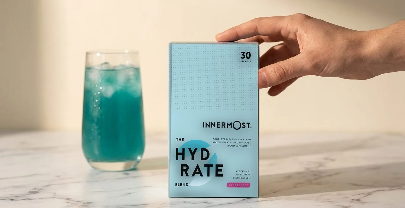 Innermost The Hydrate Blend electrolyte box in Elderberry, 30 sachets, beside a glass of blue electrolyte drink
