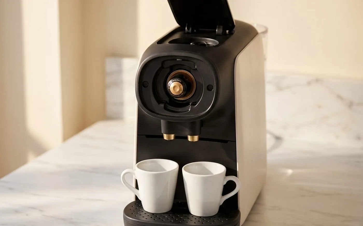 Hand removing clear water tank from L'OR Barista Sublime pod coffee machine on white marble countertop