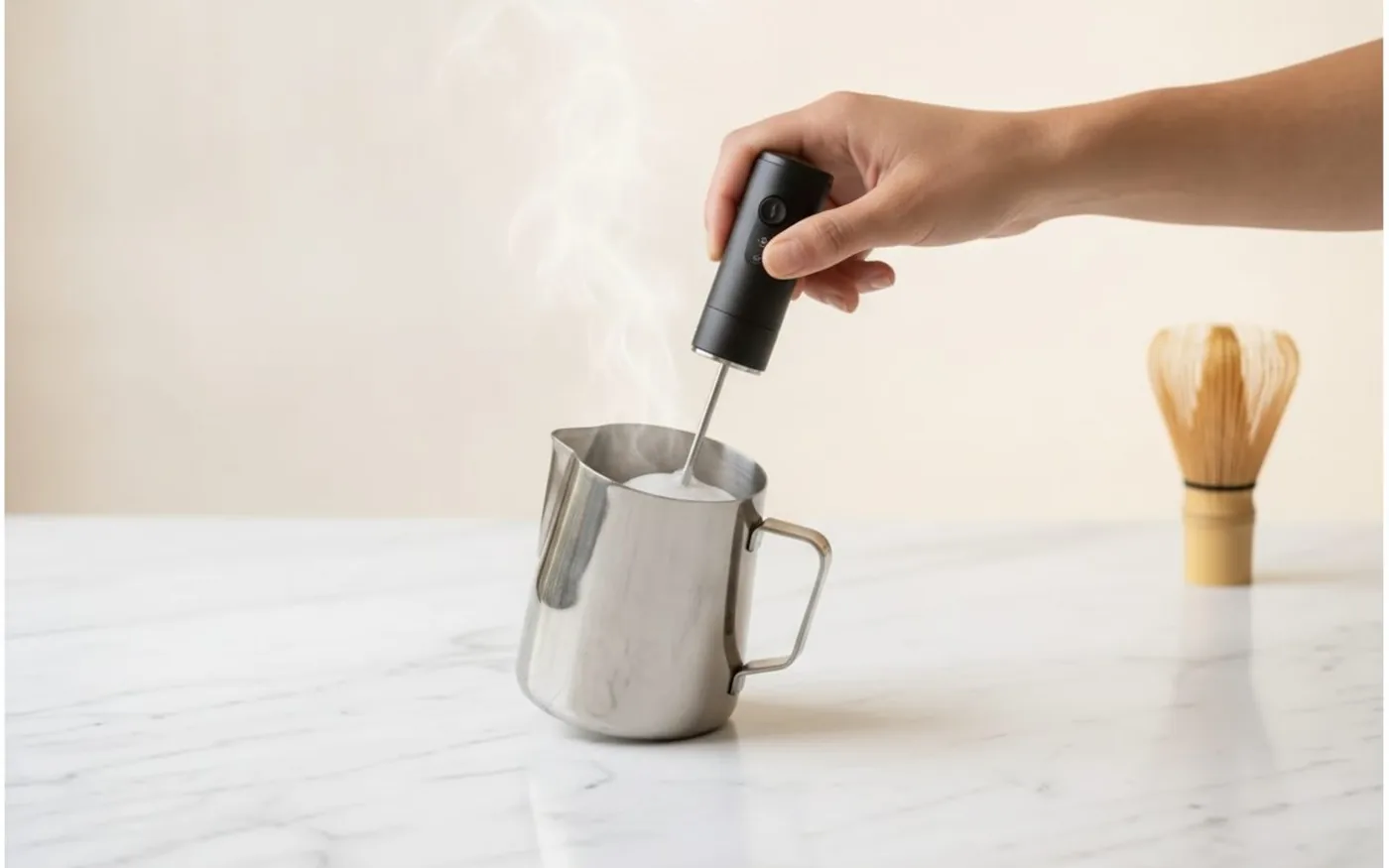 Steaming and frothing milk in a metal pitcher for a matcha latte