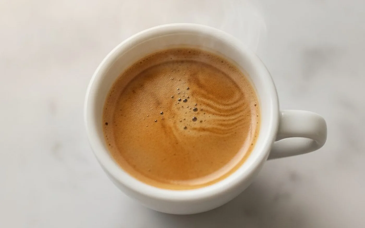 Overhead close-up of espresso crema with fine bubbles in a white cup