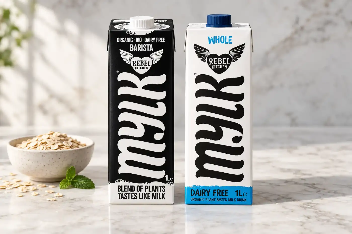 Rebel Kitchen Barista Mylk and Whole Mylk 1L cartons side by side on a marble counter beside a bowl of oats