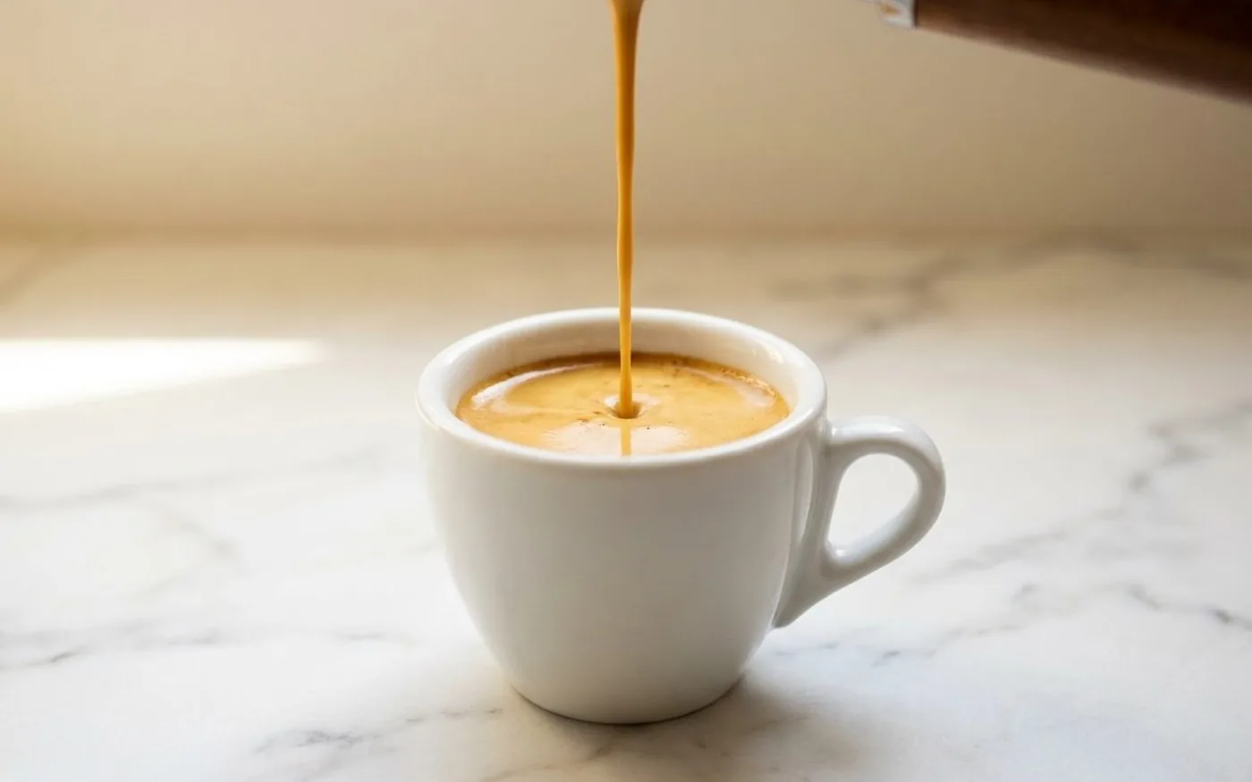 Espresso being extracted with rich golden crema into white ceramic cup on marble