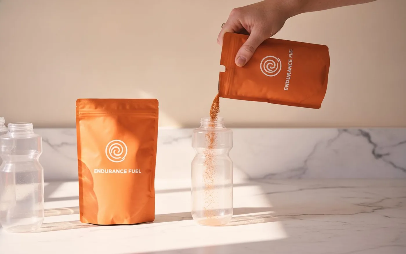 Pouring Tailwind Endurance Fuel powder into a cycling water bottle on a white marble surface