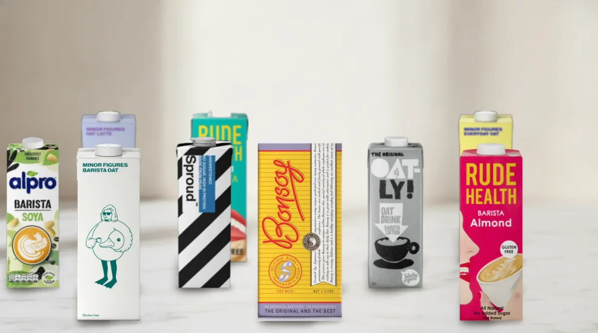 Eight real cartons of barista plant milk in three staggered rows on a white marble counter: Minor Figures Barista Oat, Bonsoy Soya Milk, Rude Health Almond Barista, Sproud, Oatly Barista, Alpro Barista Soya, Rude Health Soya Barista and Minor Figures Oat Latte